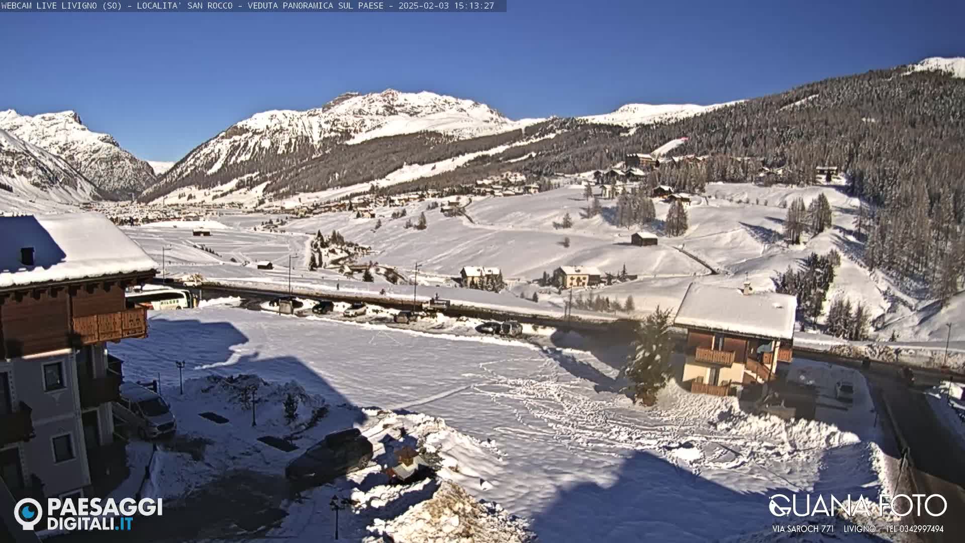 A snow-covered village nestled in a valley between snow-capped mountains under a clear blue sky.