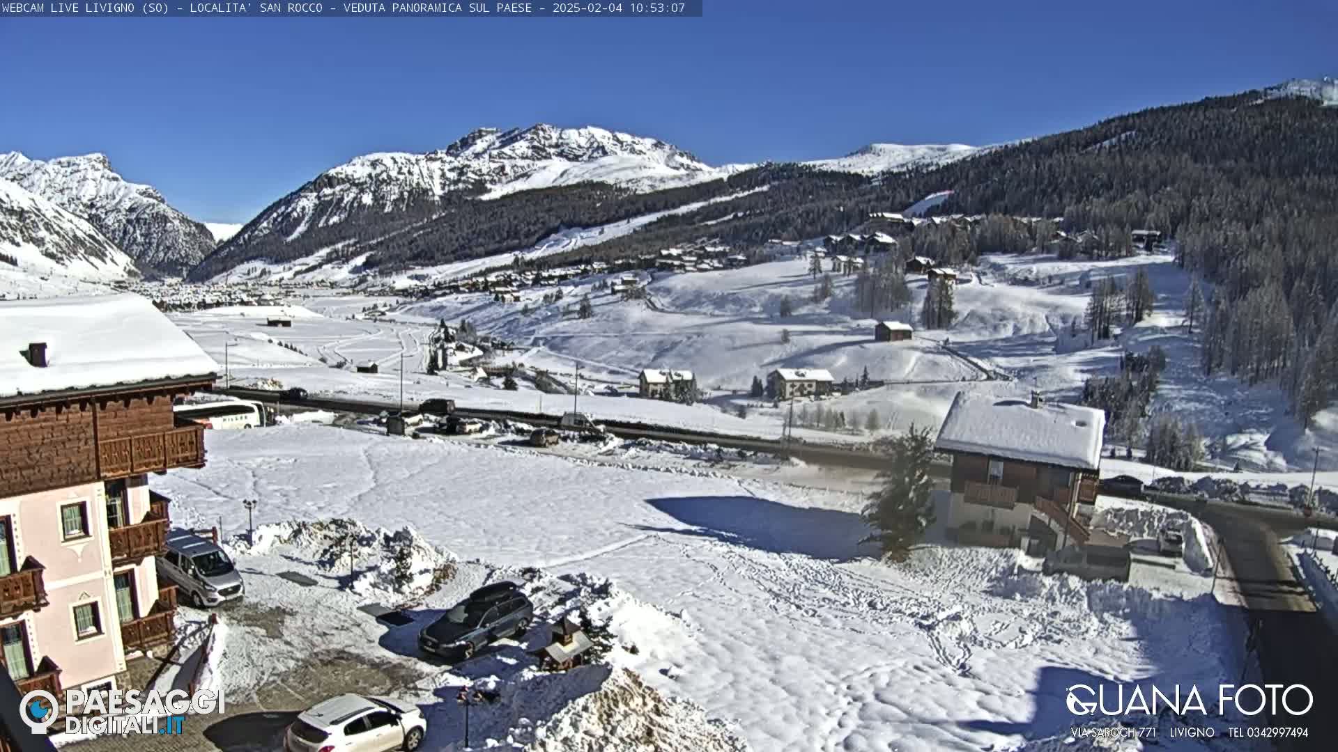 A snow-covered village nestled in a valley between snow-capped mountains under a clear blue sky.