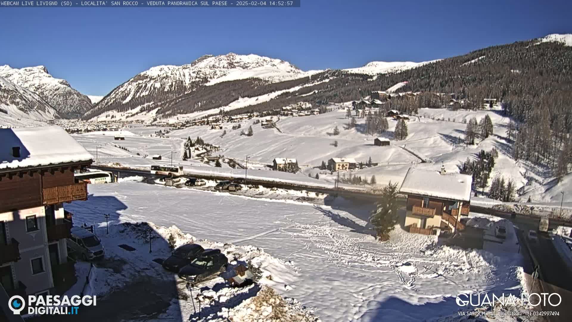 A snow-covered village nestled in a valley between snow-capped mountains under a clear blue sky.