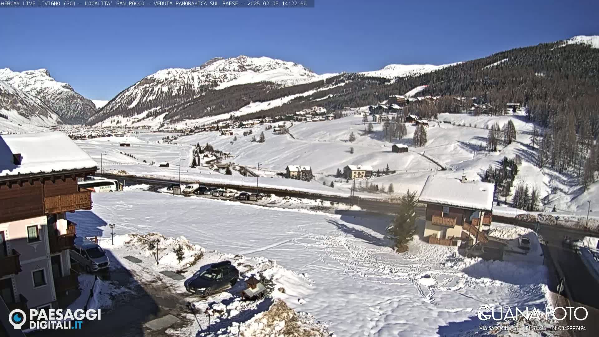 A snow-covered village nestled in a valley between snow-capped mountains under a clear blue sky.