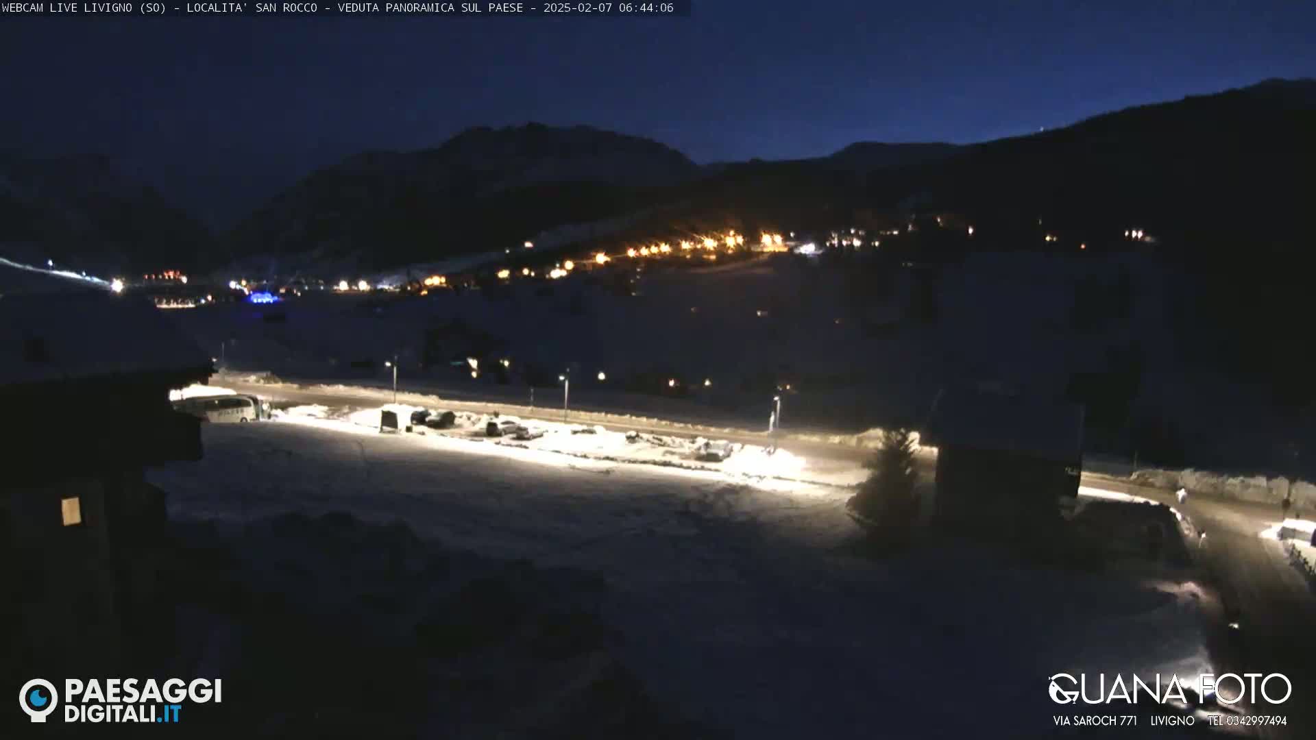 A nighttime, snow-covered mountain village is illuminated by scattered lights, with a dark, clear sky above.