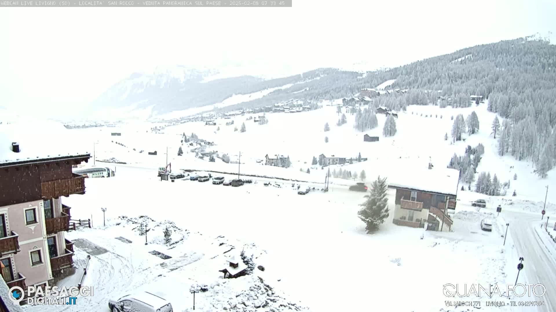 A snow-covered mountain village is seen from an elevated vantage point during a light snowfall.