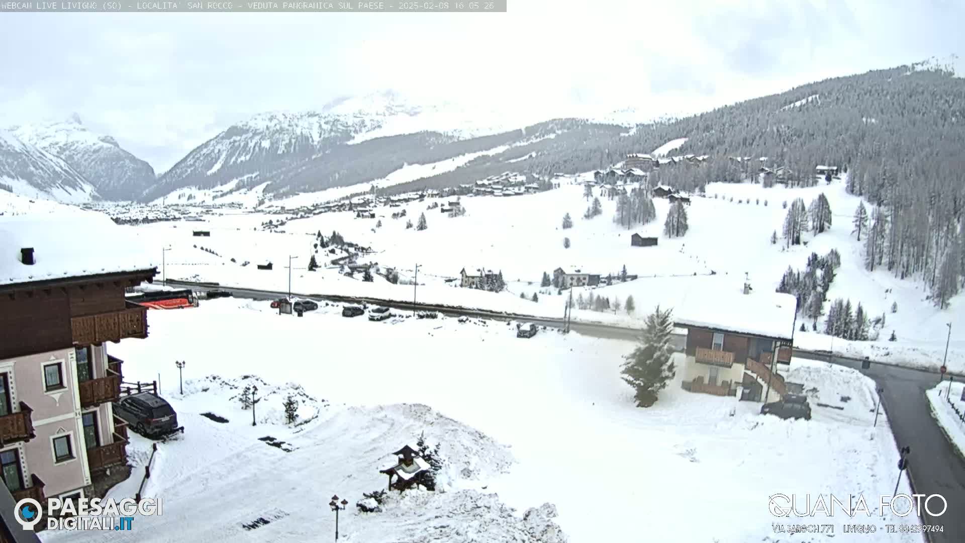 A snow-covered village nestled in a valley between snow-capped mountains under an overcast sky.