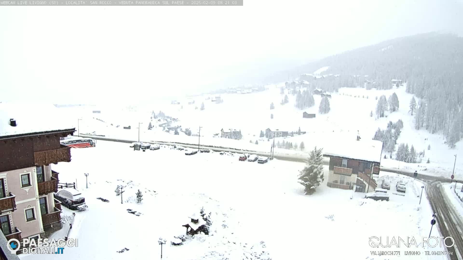 A snow-covered mountain village scene is visible, with several buildings and cars under a light snowfall.