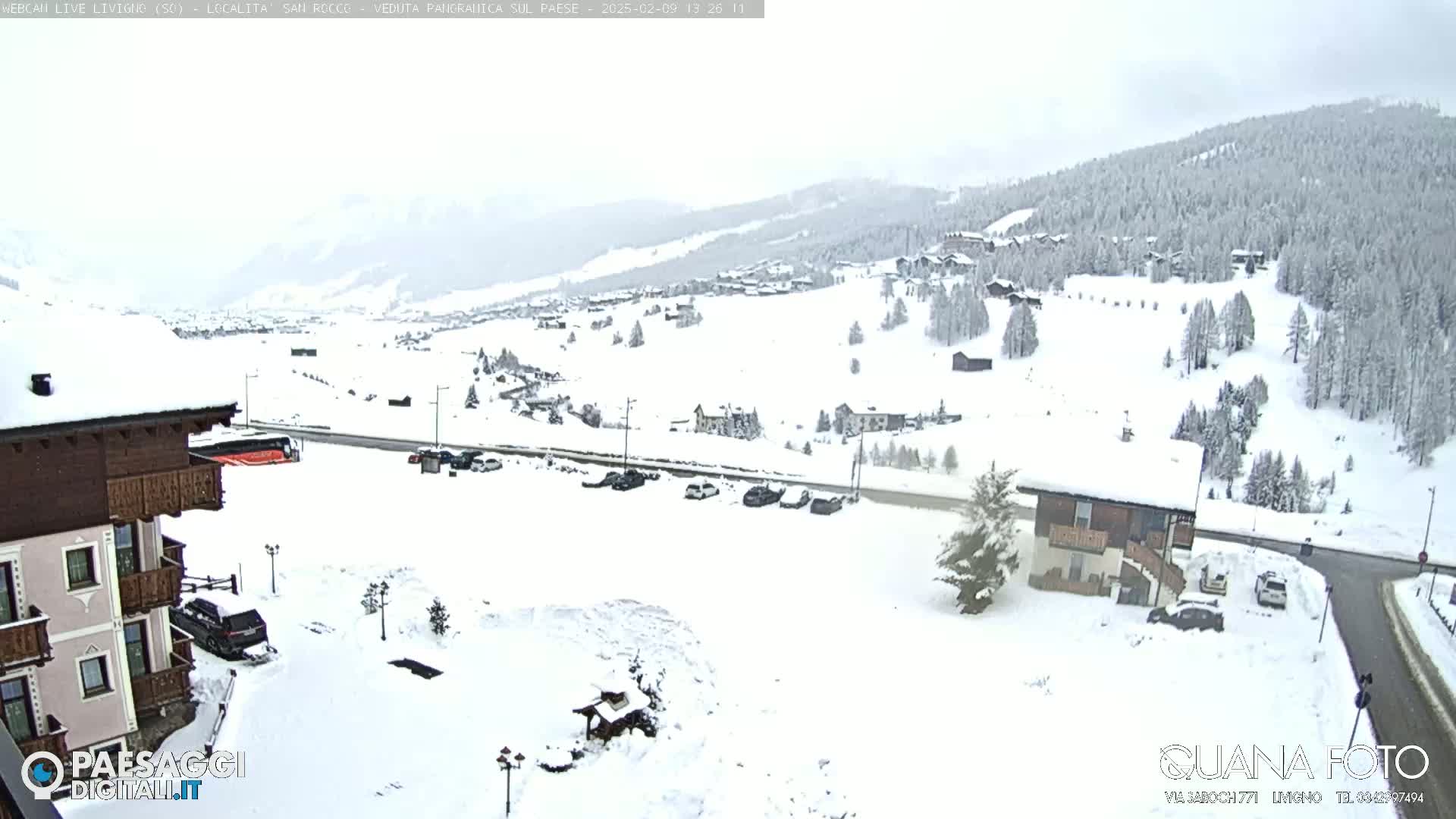 A snow-covered village nestled in a valley, with a building in the foreground and a road winding through the scene under overcast skies.