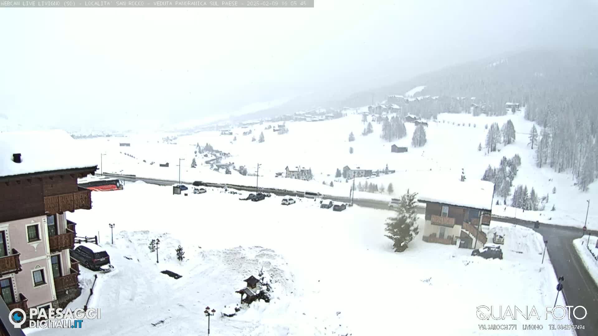 A snow-covered landscape, viewed from a building, shows a town nestled in a valley under a heavy, overcast sky.