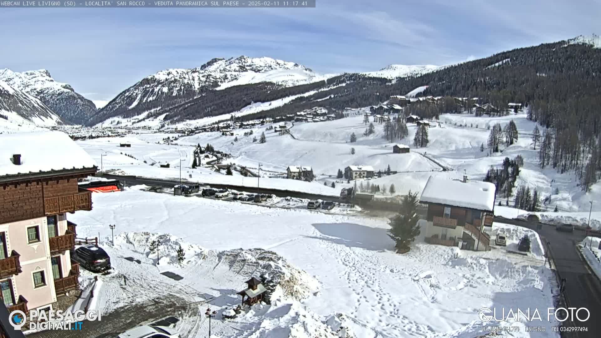 A snow-covered village nestled in a valley between snow-capped mountains under a sunny sky.