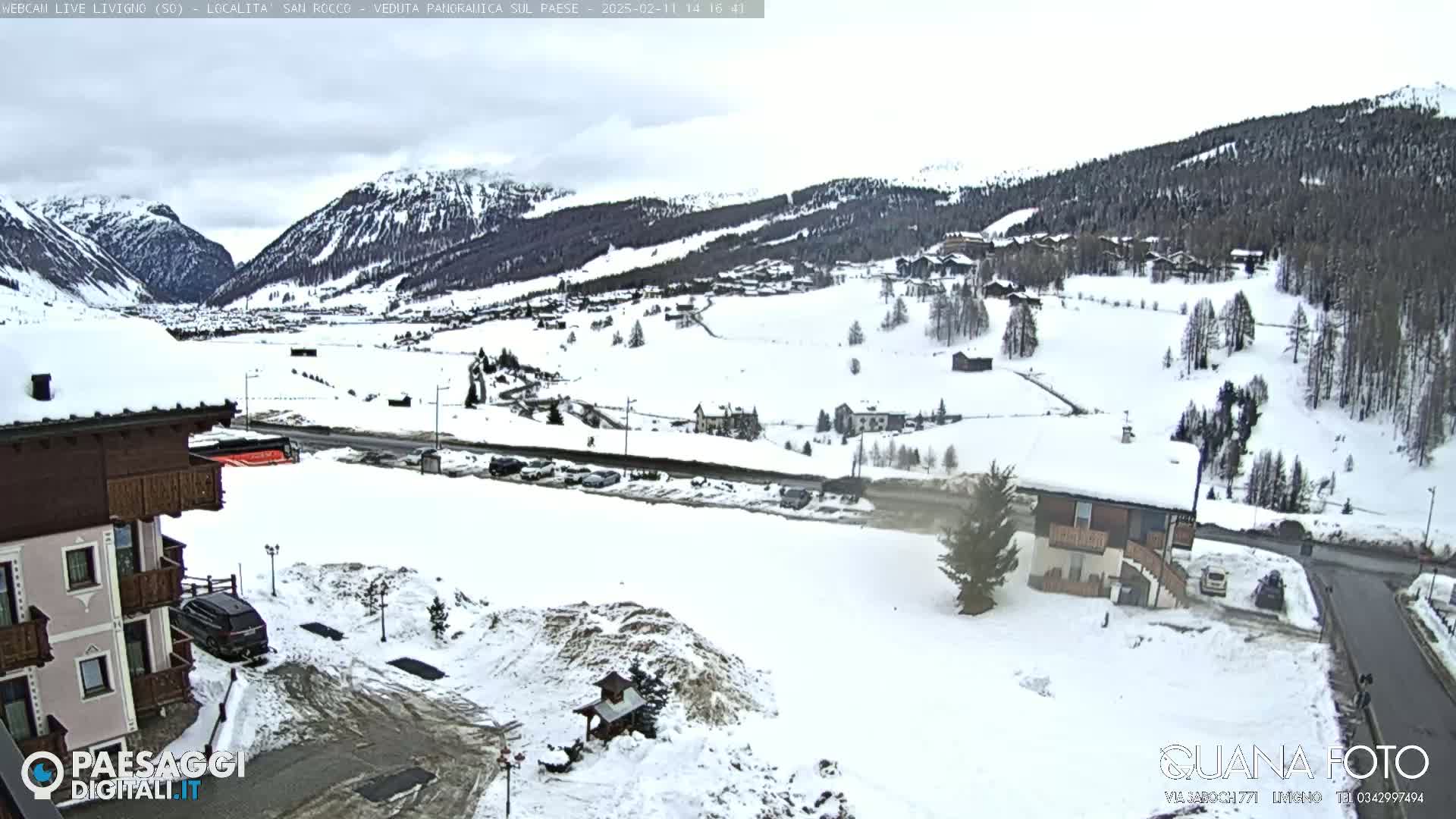 A snow-covered valley scene with buildings and a road, viewed from a slightly elevated position on an overcast day.
