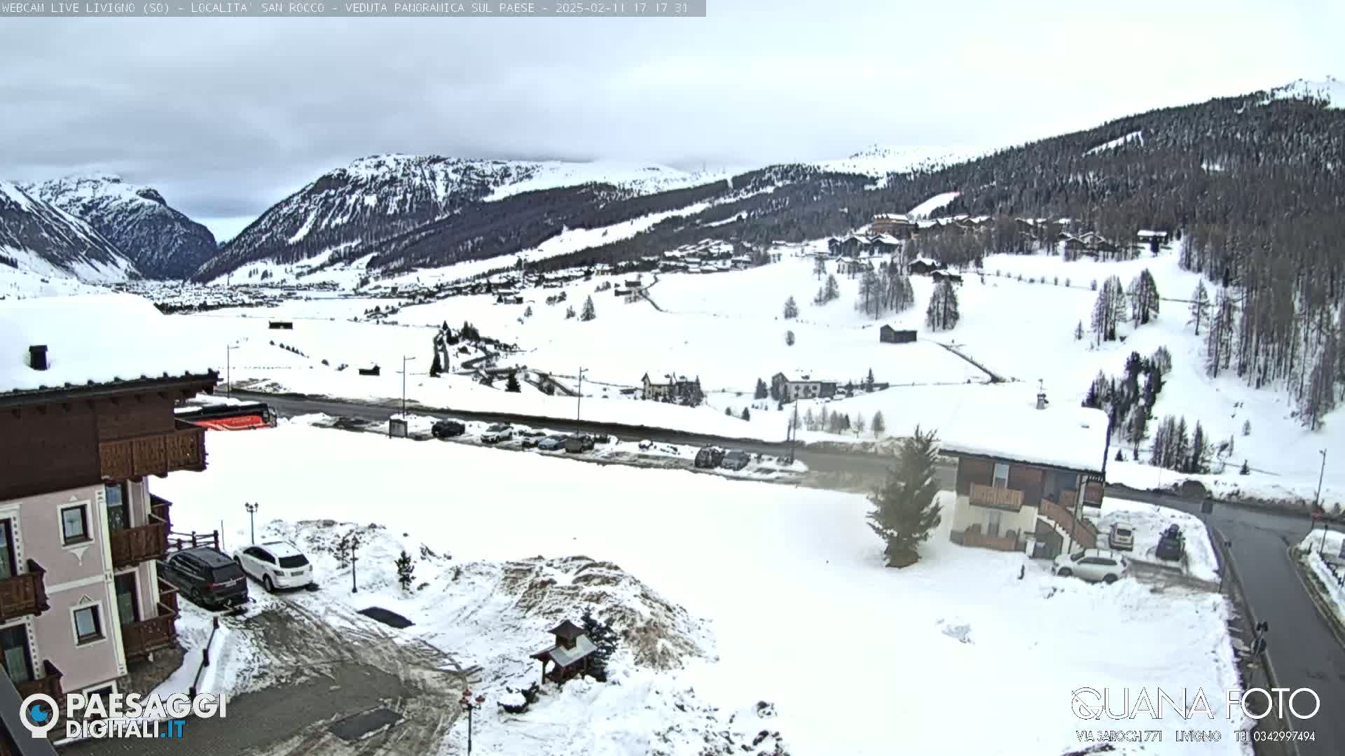 A snow-covered mountain valley scene with buildings, cars, and overcast skies.