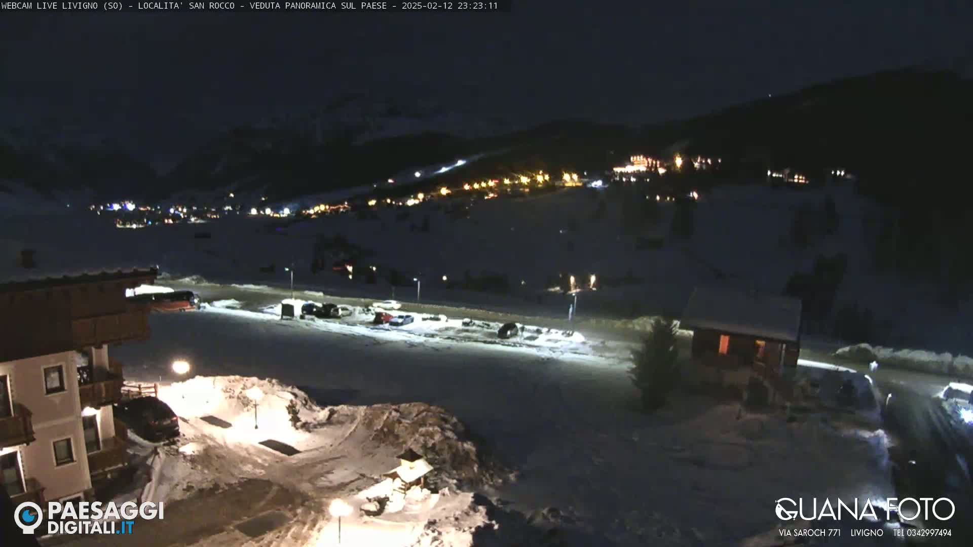 A nighttime view of a snow-covered village in a mountainous region, illuminated by scattered lights.
