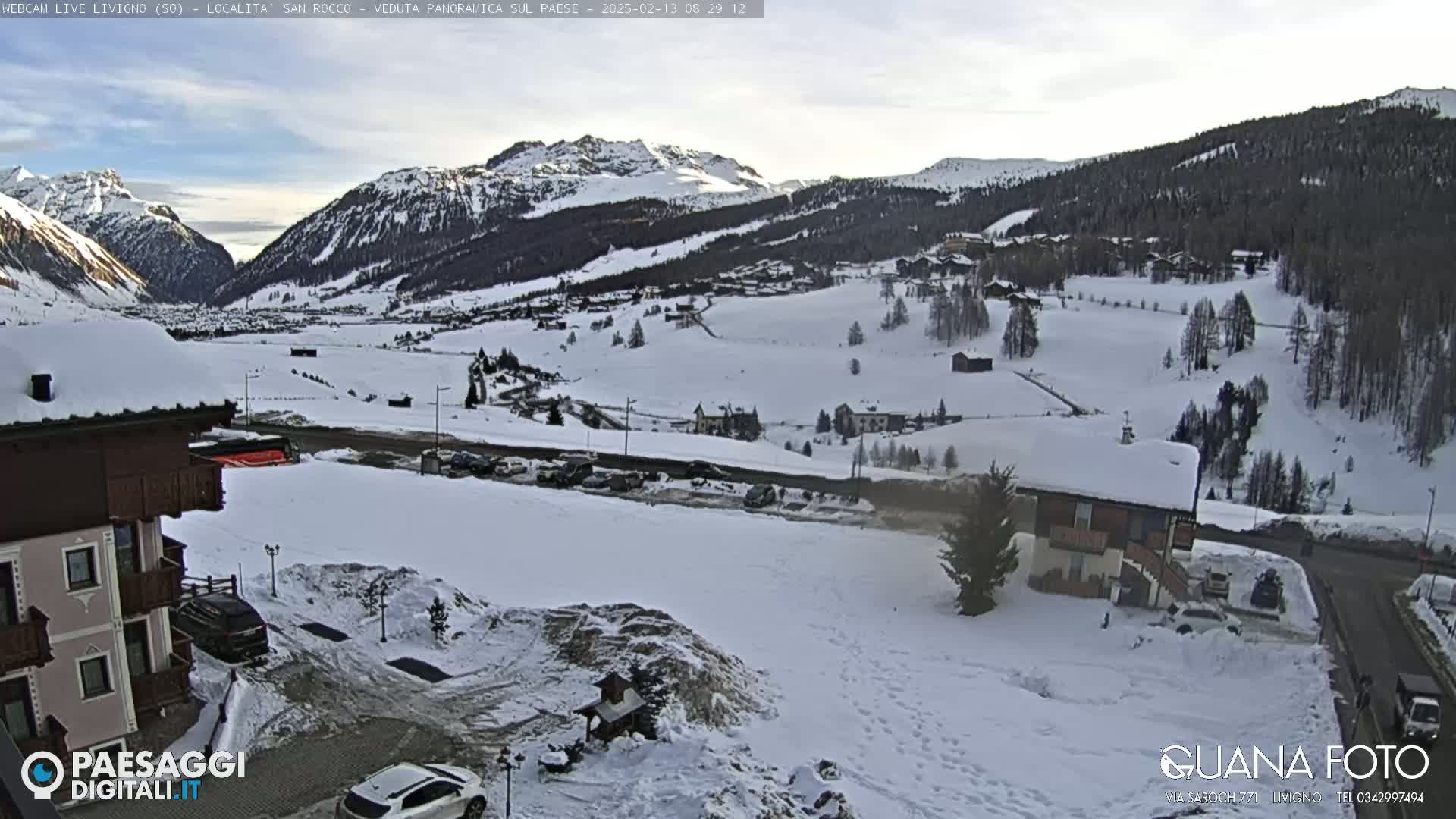 A snow-covered mountain valley scene, with a village nestled amongst the hills under a partly cloudy sky.
