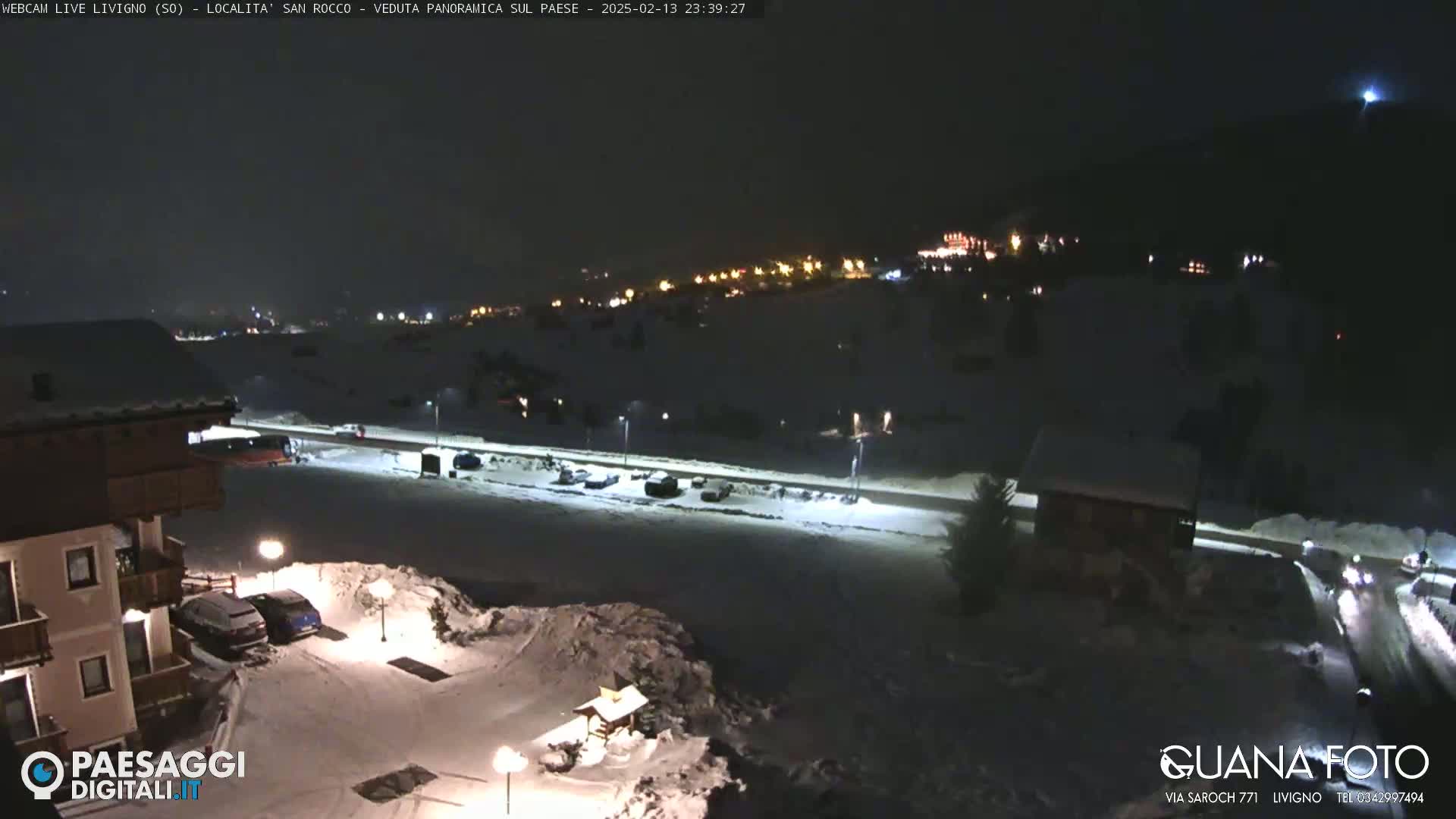 A snow-covered town is illuminated at night by streetlights and building lights, under a clear, dark sky.