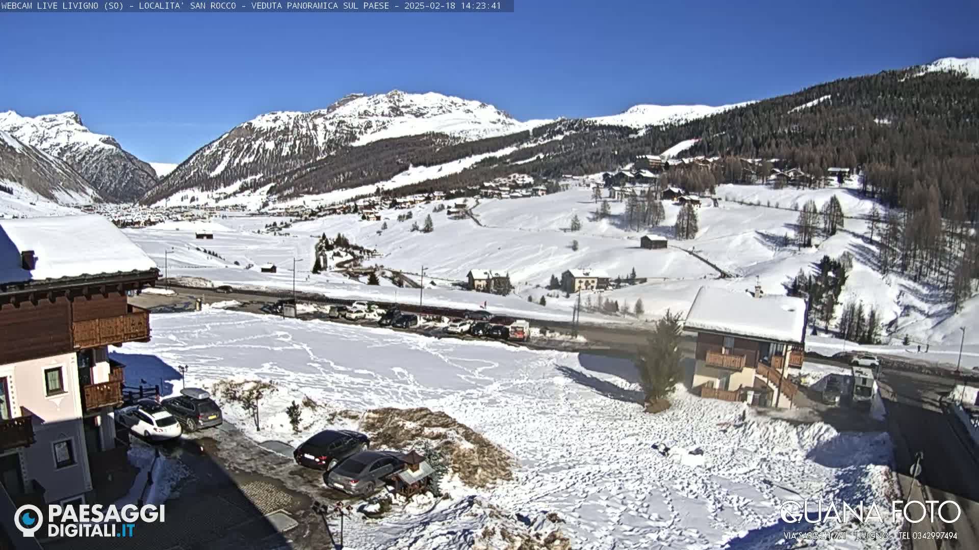 A snow-covered village nestled in a valley between snow-capped mountains under a clear blue sky.