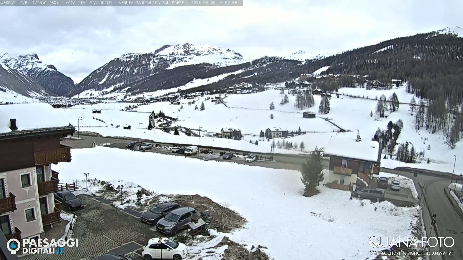 A snow-covered mountain valley scene with several buildings, cars in parking lots, and a road.