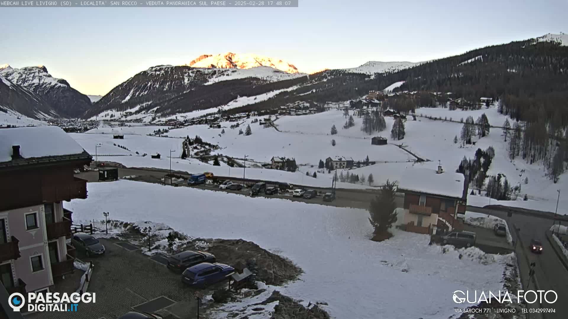 A snow-covered valley with mountains in the background, under a twilight sky.