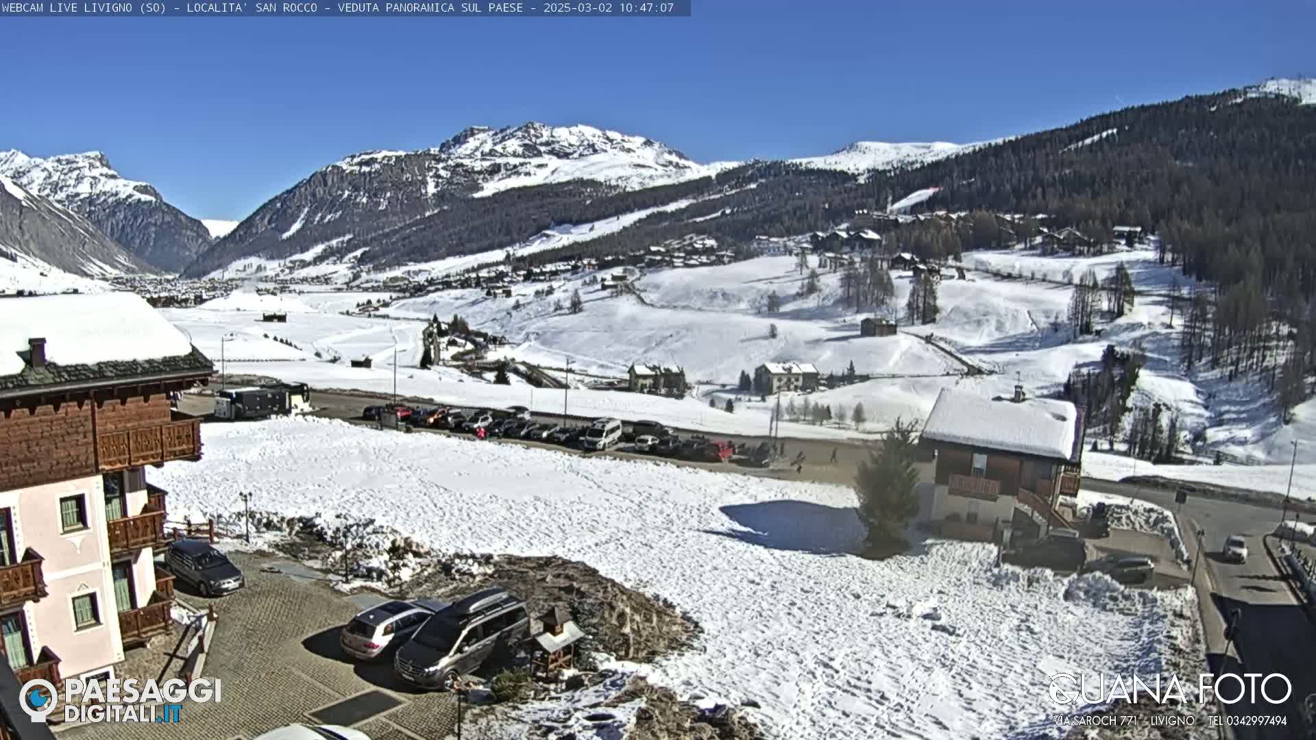 A snow-covered village nestled in a valley between snow-capped mountains on a sunny day.
