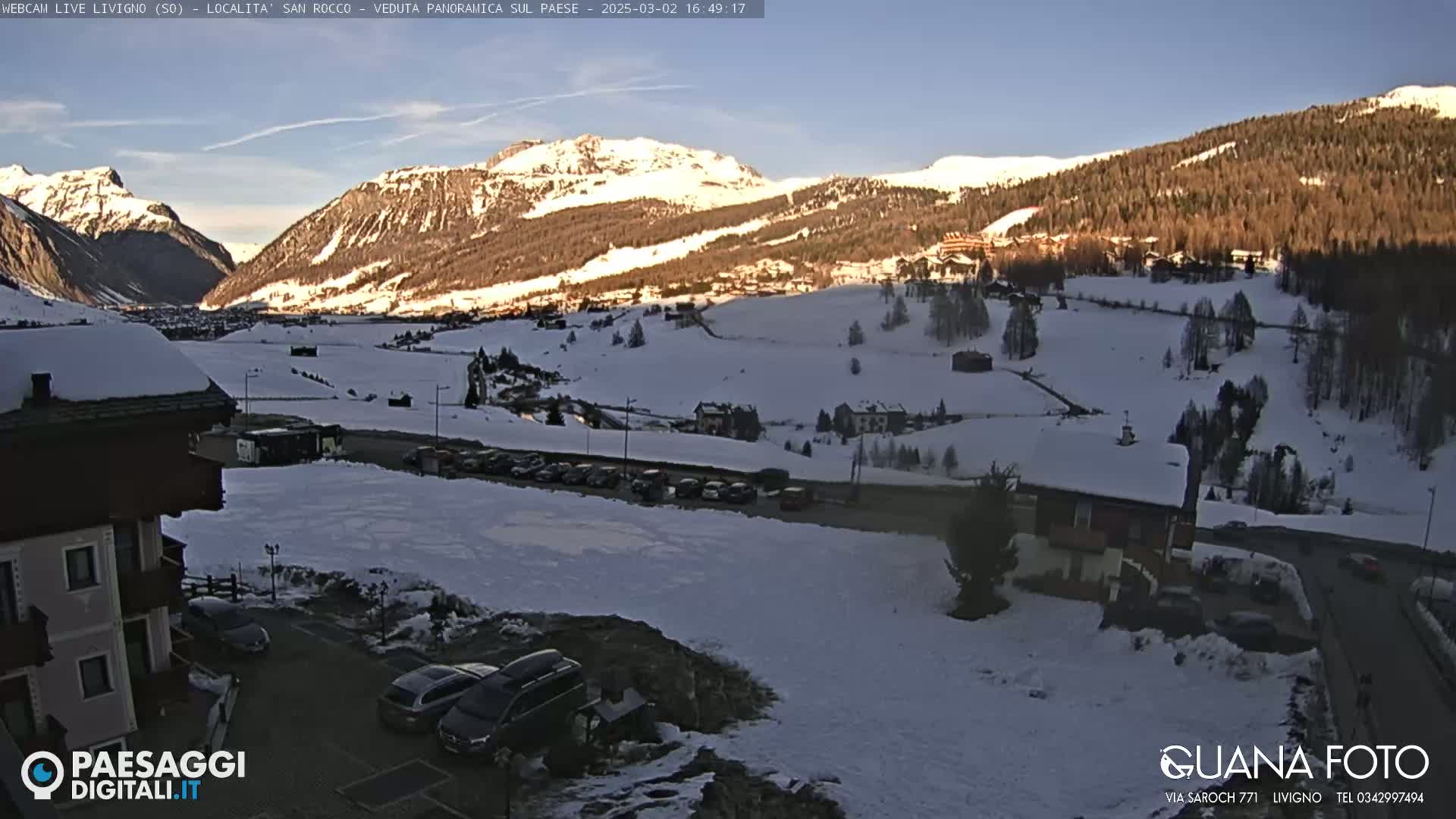 A snow-covered mountain valley scene is visible under a clear blue sky, with a few cars parked near a building in the foreground.