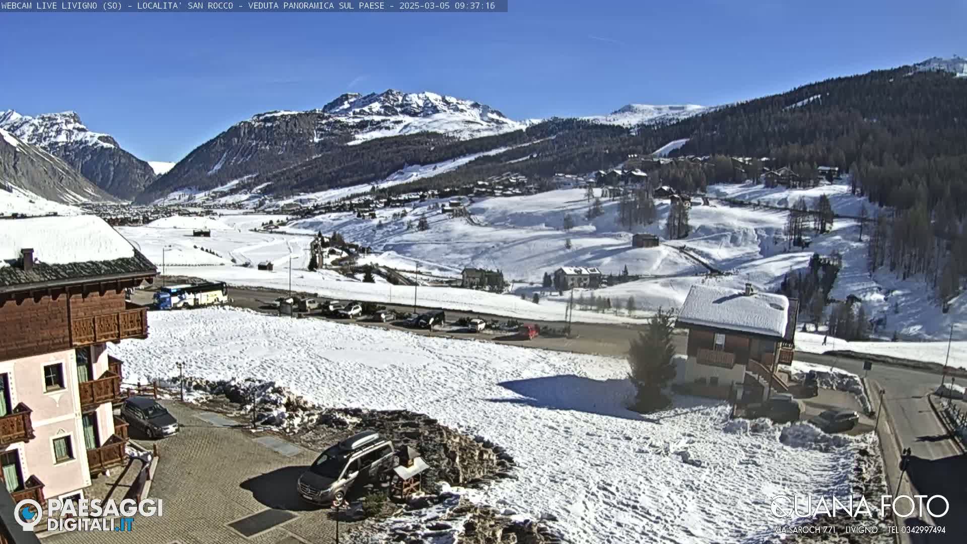 A snow-covered village nestled in a valley between snow-capped mountains under a clear blue sky.
