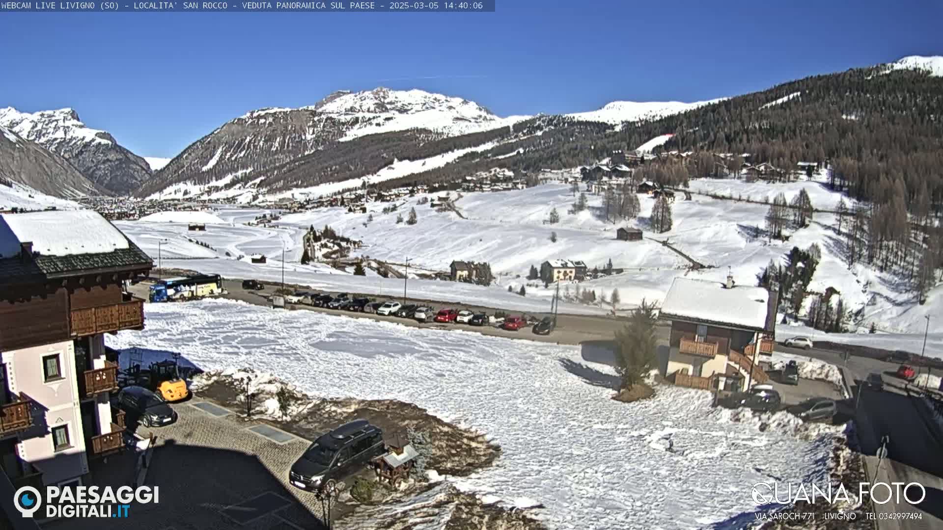A snow-covered village nestled in a valley between snow-capped mountains on a sunny day.