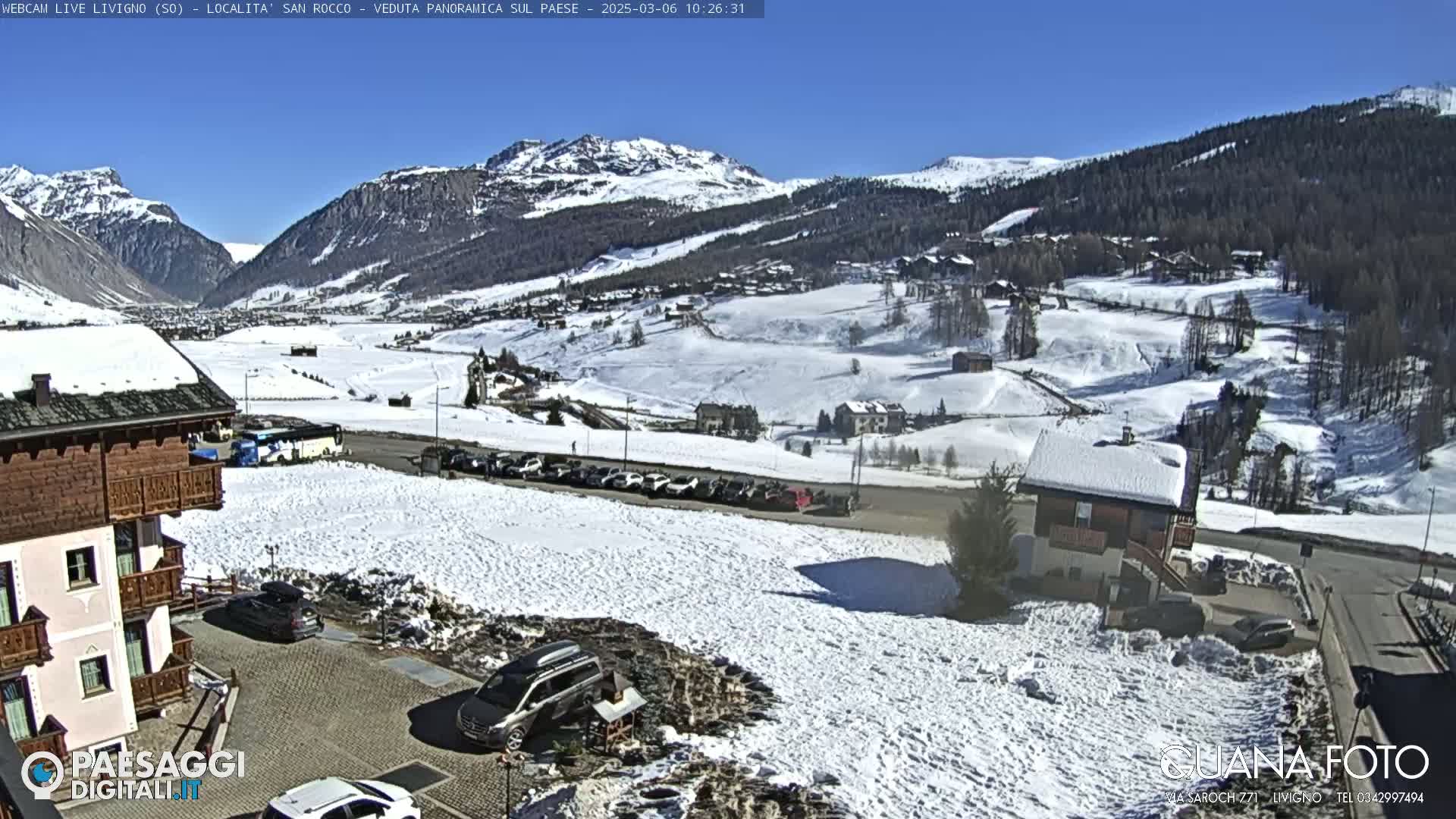 A snow-covered village nestled in a valley between snow-capped mountains under a clear blue sky.