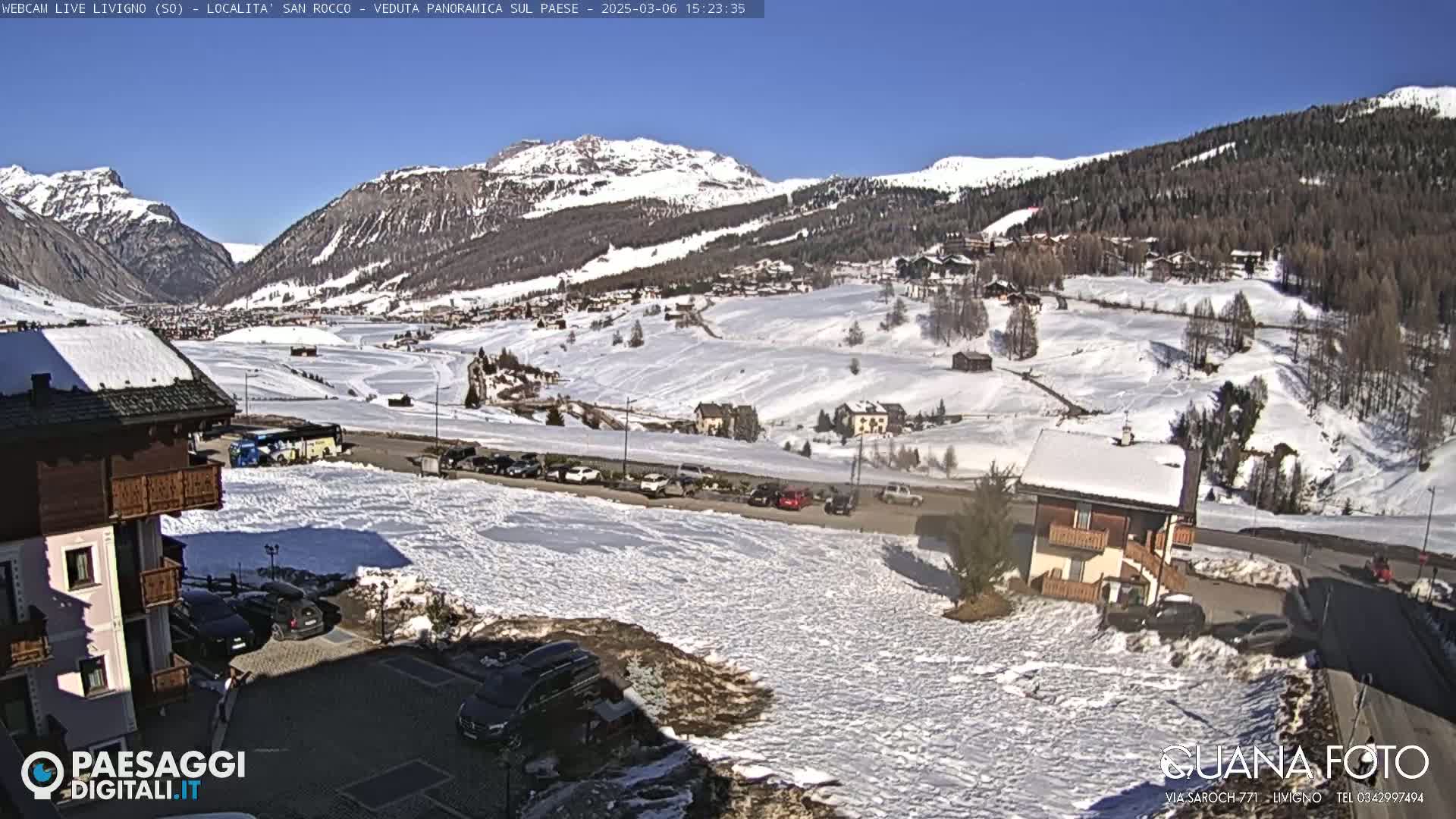 A snow-covered valley town is nestled among snow-capped mountains under a clear blue sky.