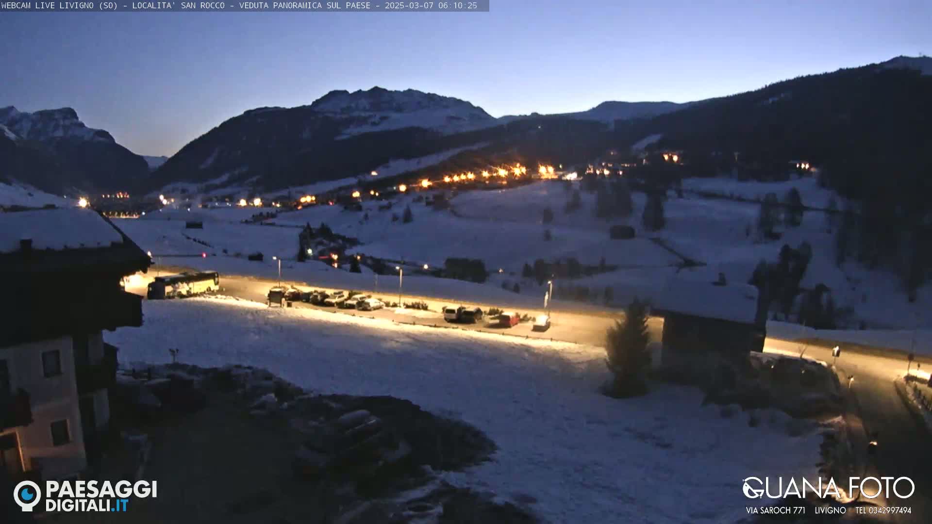 A snow-covered mountain village is illuminated at night under a twilight sky.