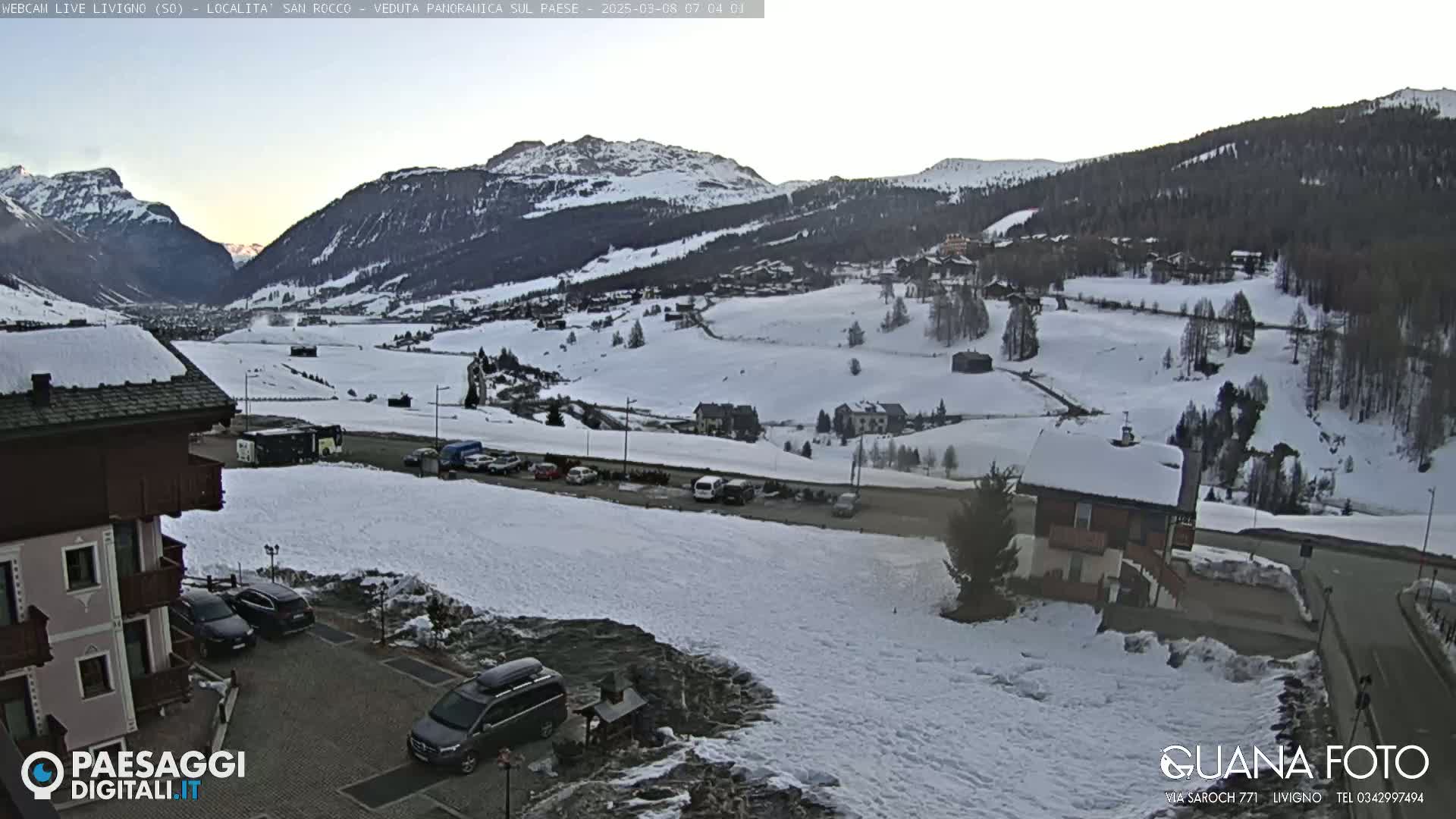 A snow-covered mountain valley village scene under a clear, light sky.