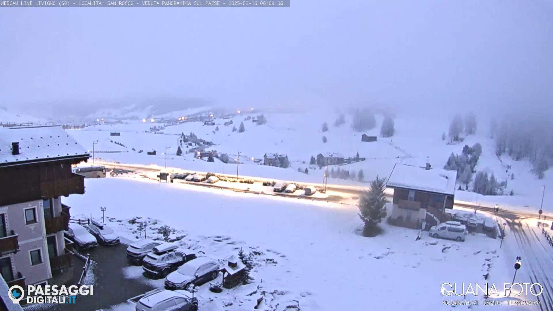 A snow-covered landscape with buildings, cars, and a road is visible under a hazy, light sky.