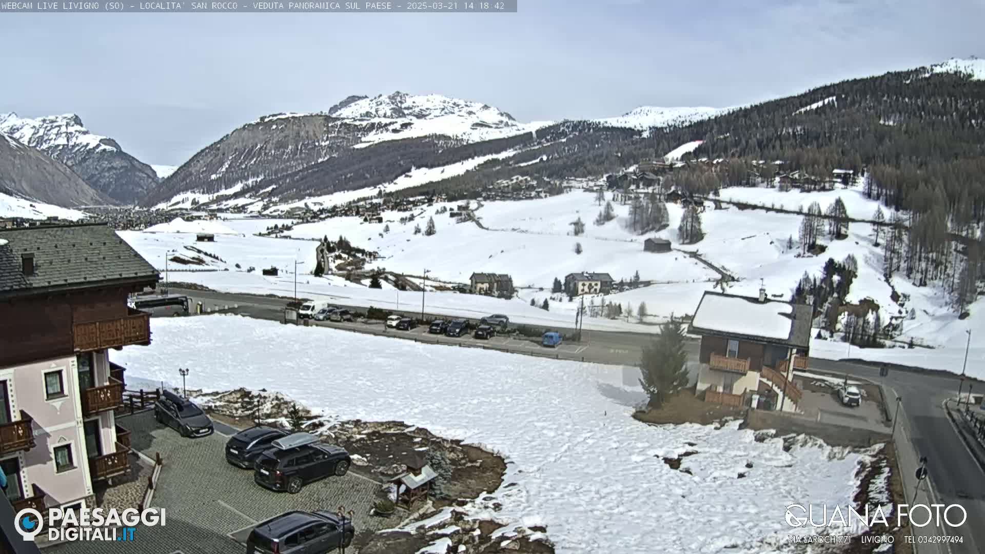 A snow-covered mountain valley with buildings and cars, under a mostly clear sky.