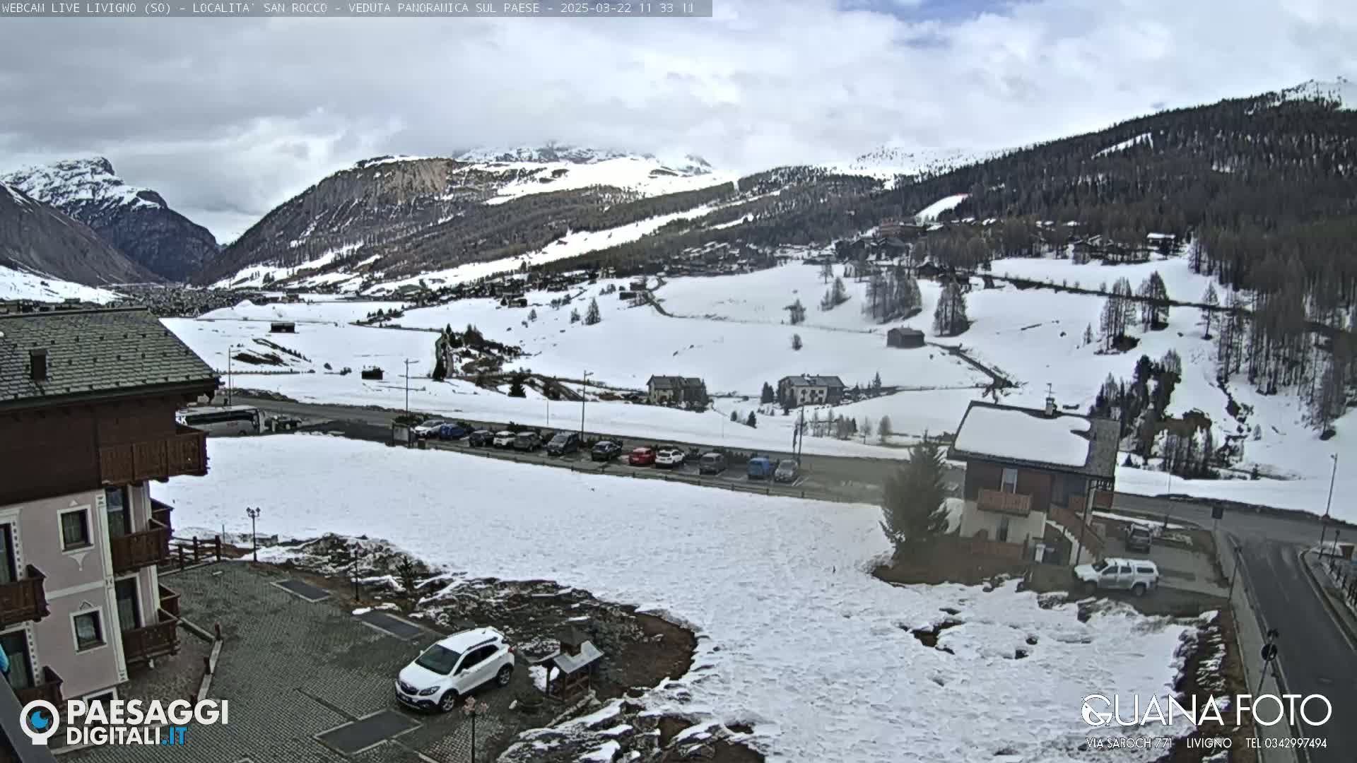 A snow-covered mountain valley with buildings and a parking lot, under a cloudy sky.