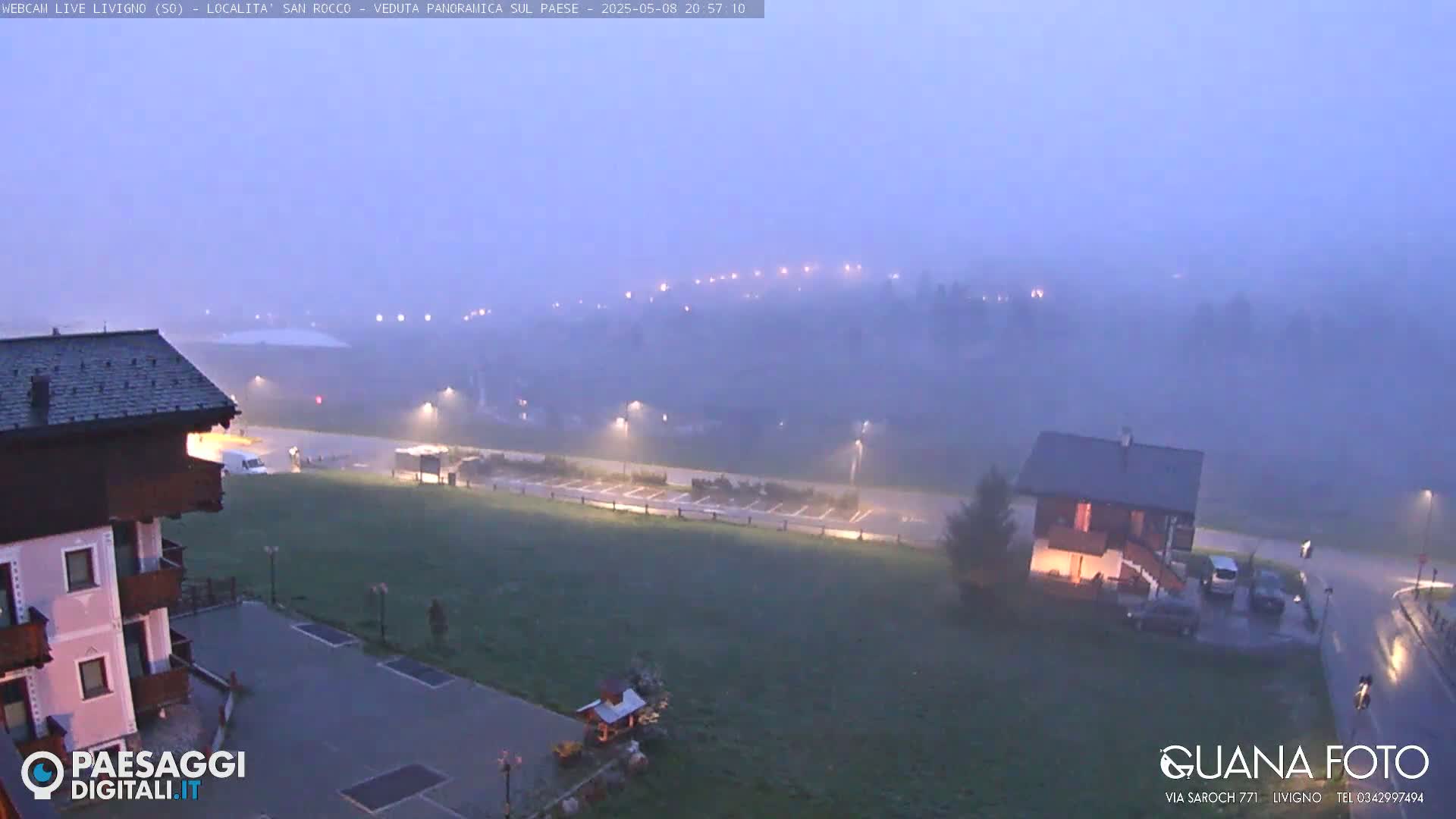 A foggy, dimly lit mountain town scene at dusk shows a parking lot, buildings, and a few cars.
