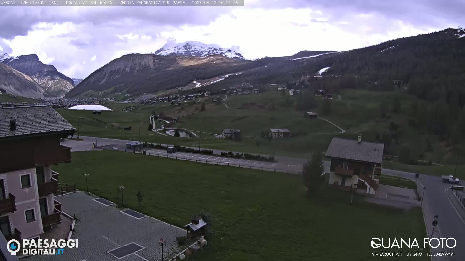 A mountain valley town is visible under an overcast sky, with a snow-capped mountain in the background.