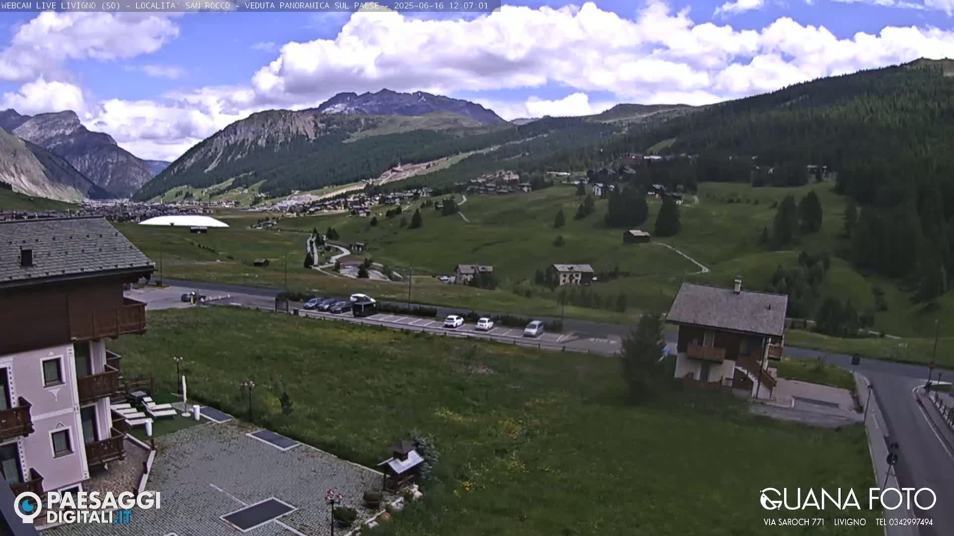 A mountain valley town is visible under a partly cloudy sky, with several buildings, cars, and green spaces.