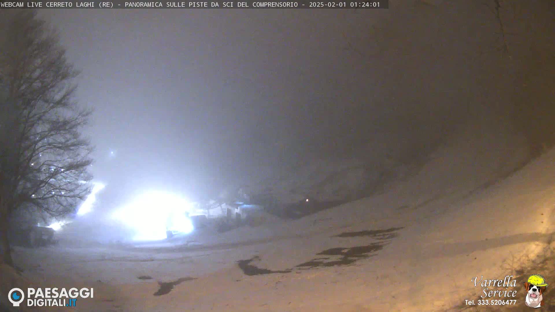 A snowy, foggy night scene shows a brightly lit area in the mid-ground and a dark, snow-covered landscape extending to the foreground.
