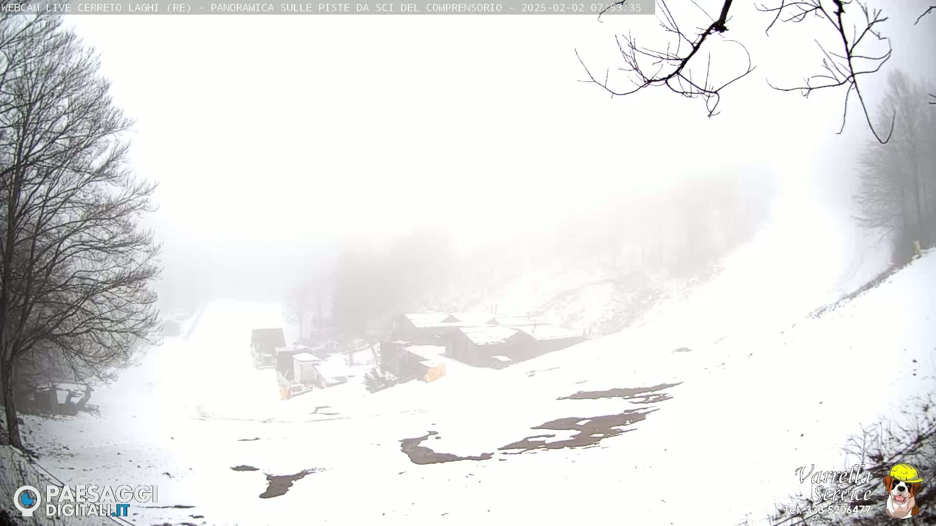 A snow-covered hillside with a few buildings in the distance is shrouded in fog.