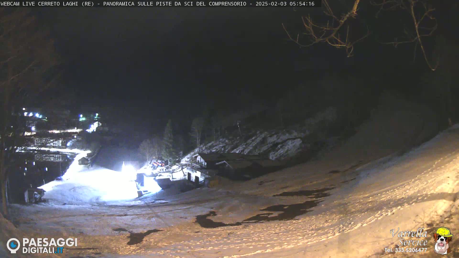 A nighttime view of a snow-covered ski slope with a building and some lights visible in the distance.