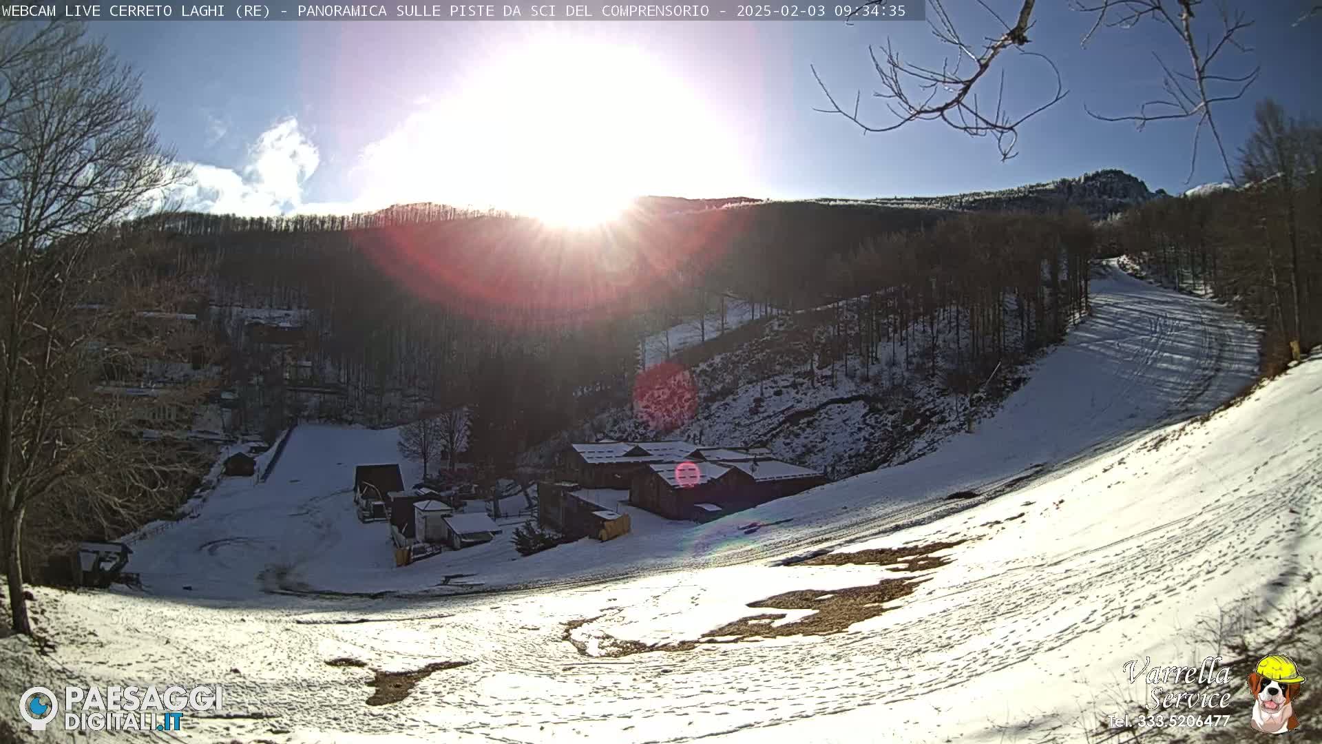 A snow-covered ski slope with buildings below, under a bright, sunny sky.