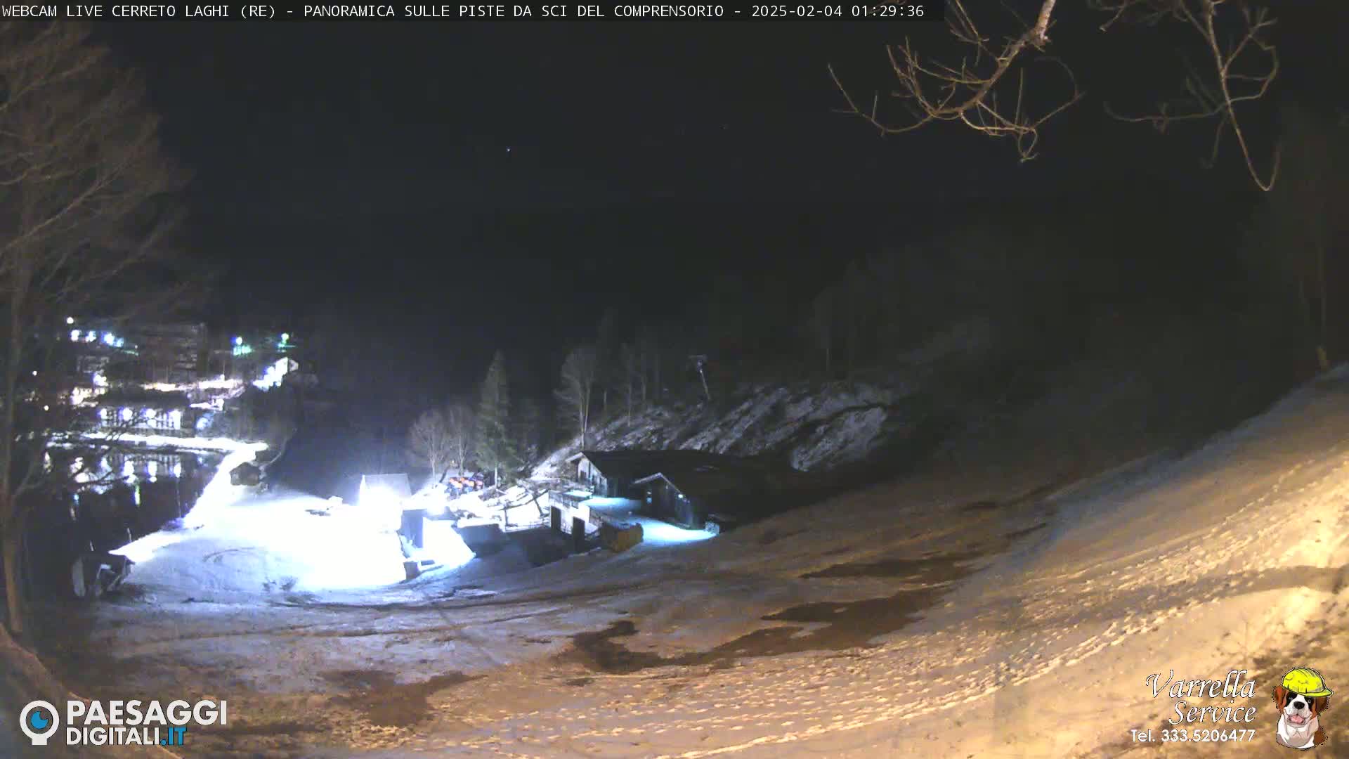 A nighttime view of a snow-covered ski slope with illuminated buildings and trees in the background.