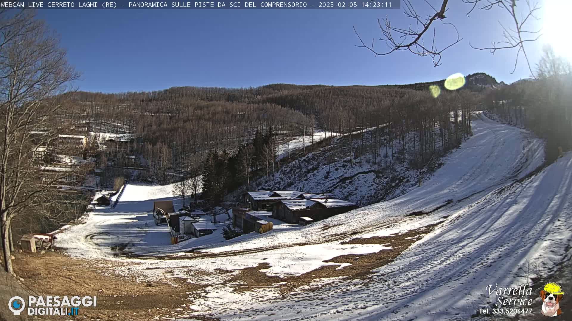 A snow-covered ski slope with a cluster of buildings at its base under a bright, sunny sky.