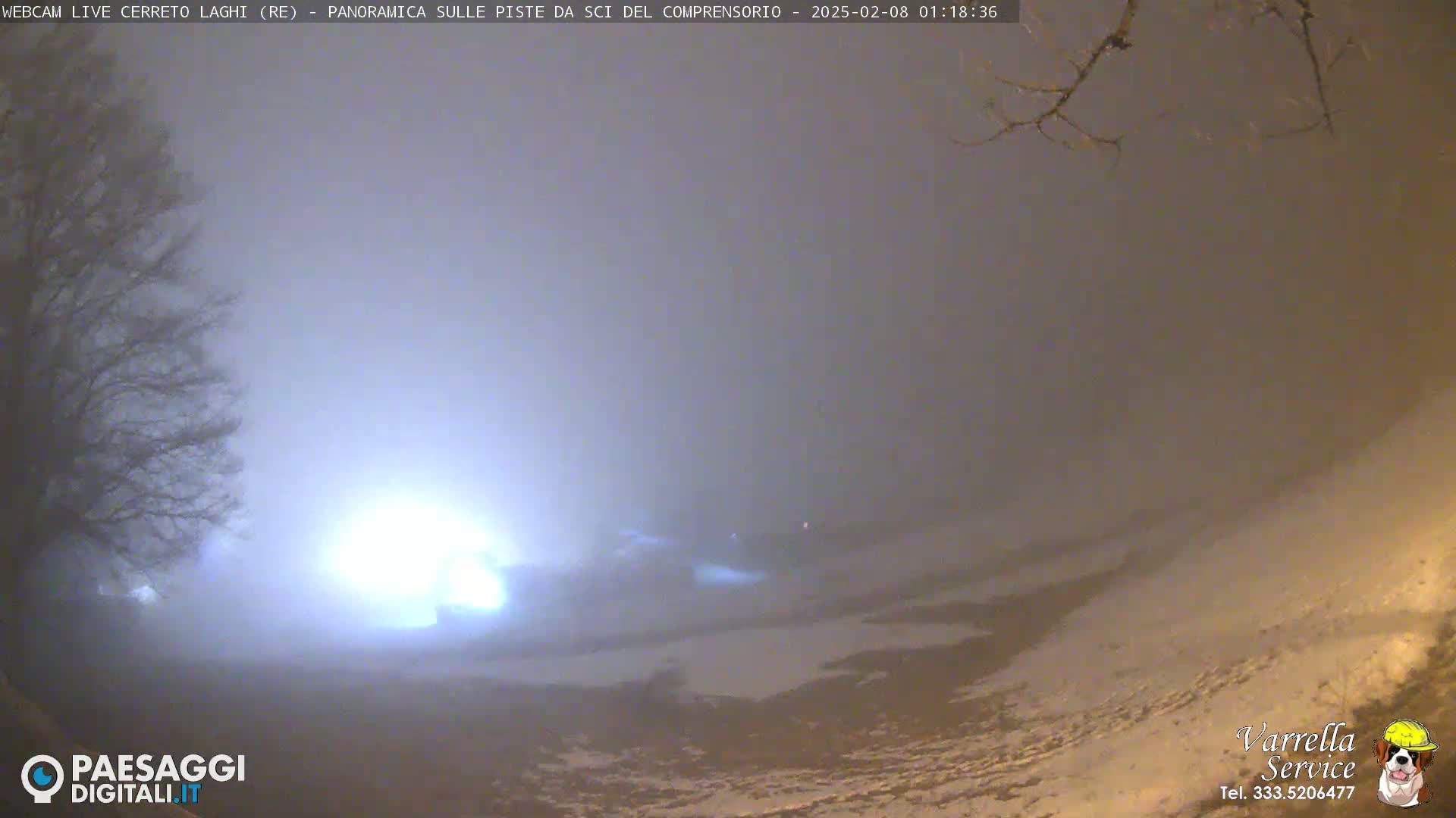 A foggy, snowy landscape at night is illuminated by a bright light source in the distance.