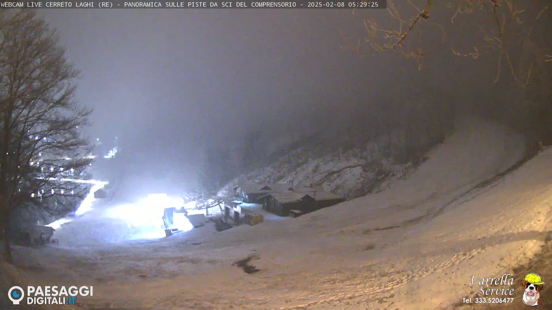 A snow-covered ski slope at night is illuminated by bright lights, with a foggy atmosphere.