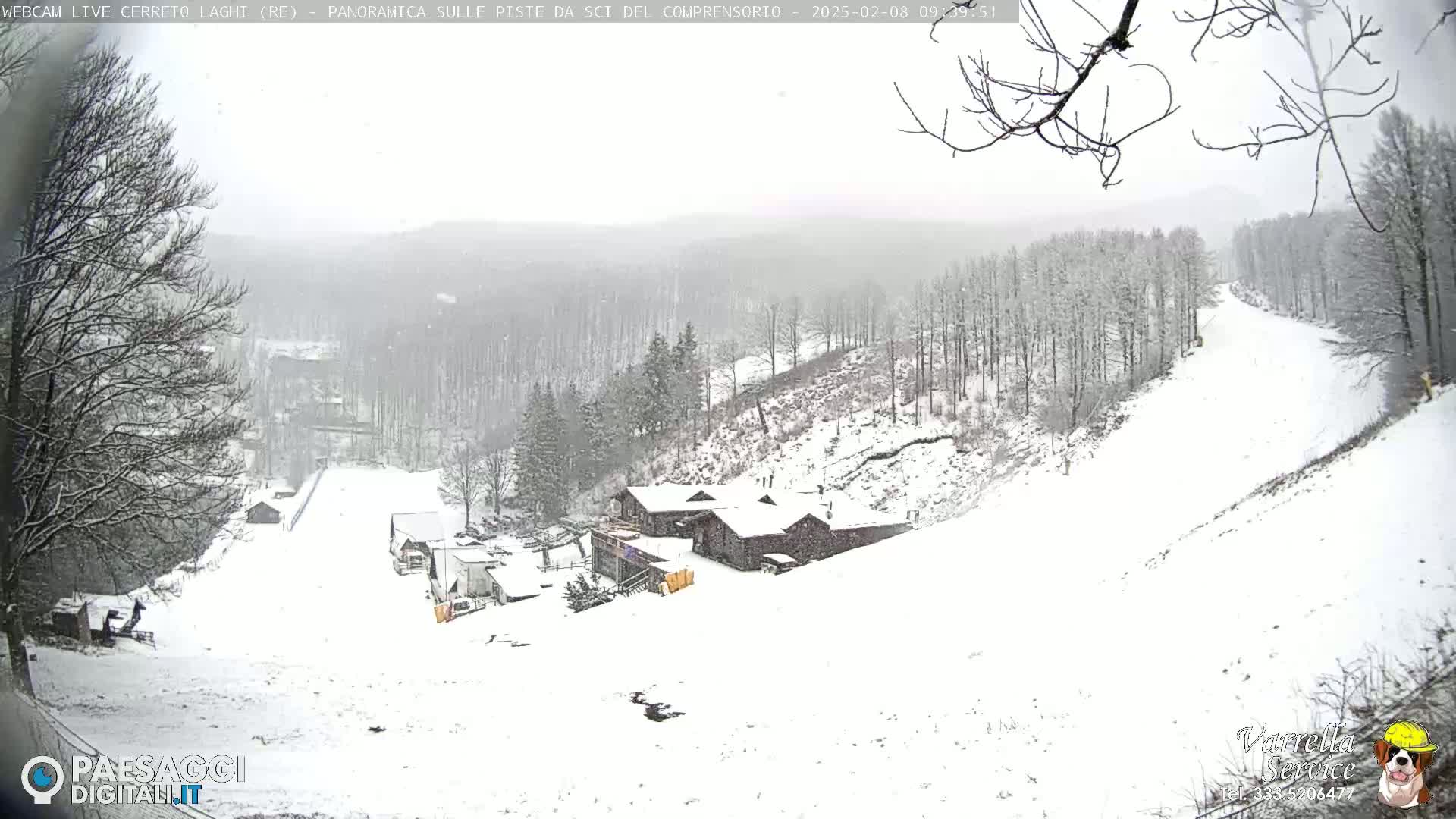A snow-covered ski slope with a building and trees in the background during a light snowfall.