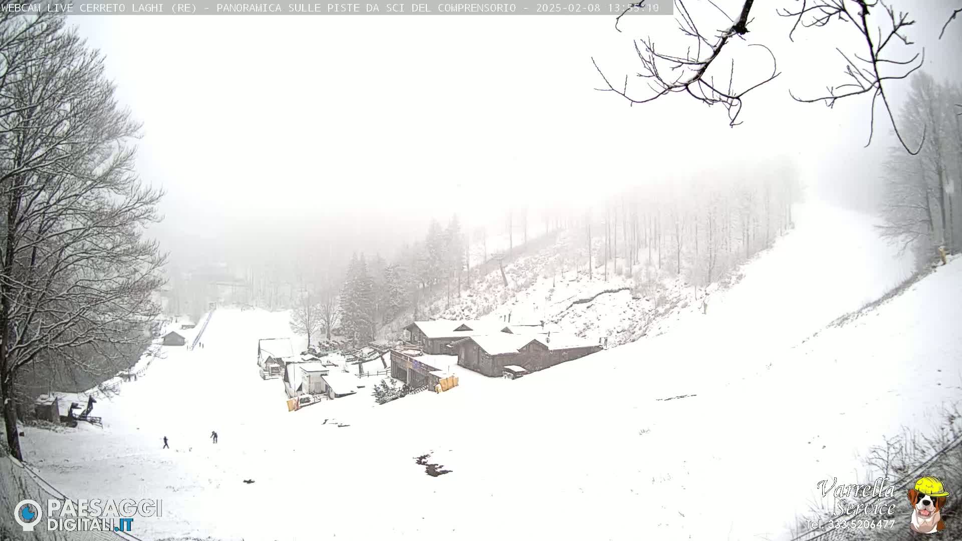 A snow-covered ski slope with several buildings and a few people visible in the distance, under a hazy, snowy sky.