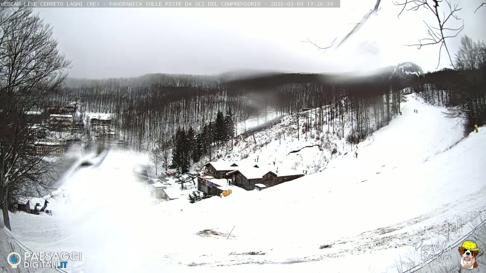 A snow-covered ski slope with a building and trees in the background under an overcast sky.