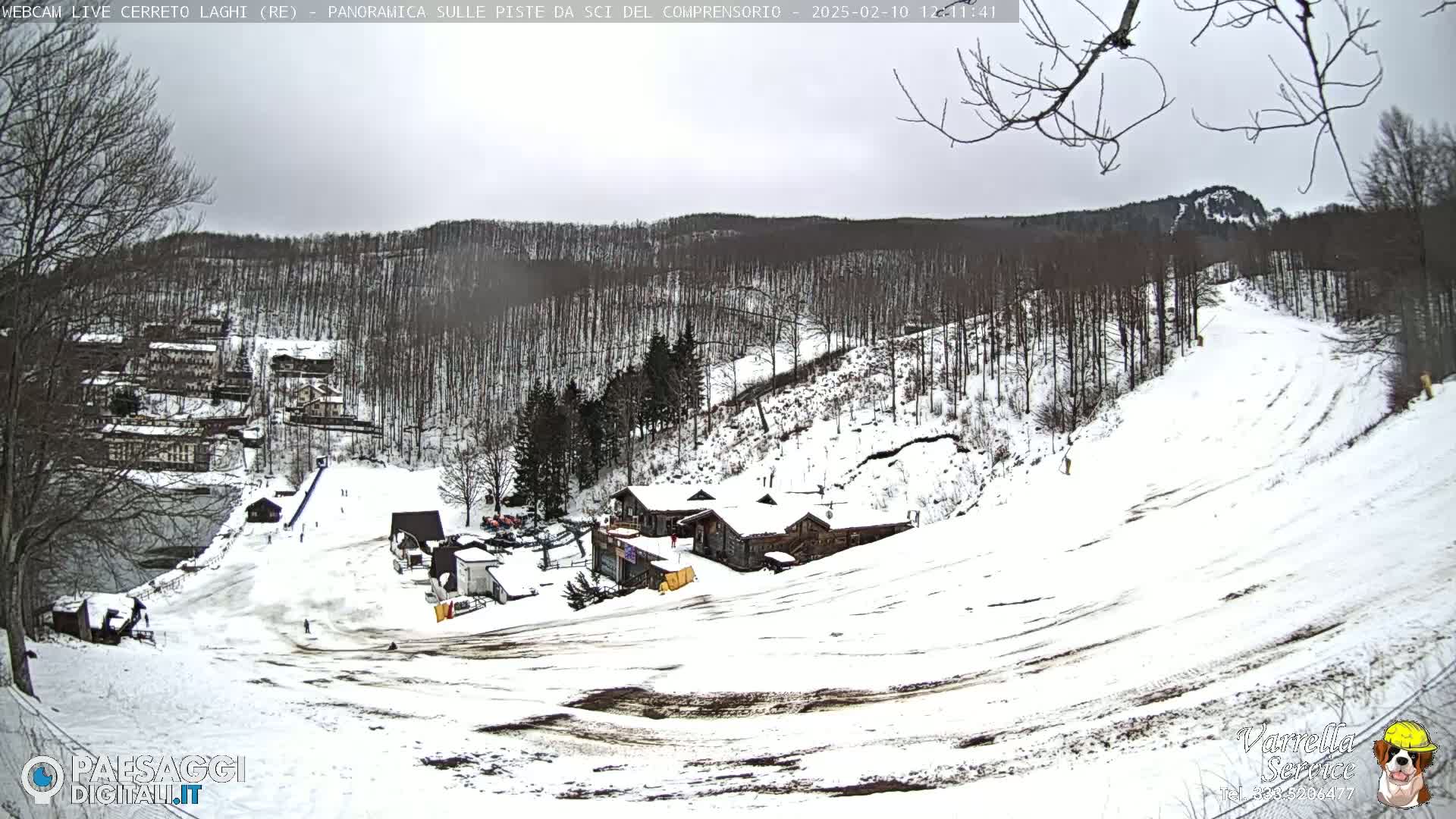 A snow-covered ski slope with a few buildings and trees under an overcast sky.