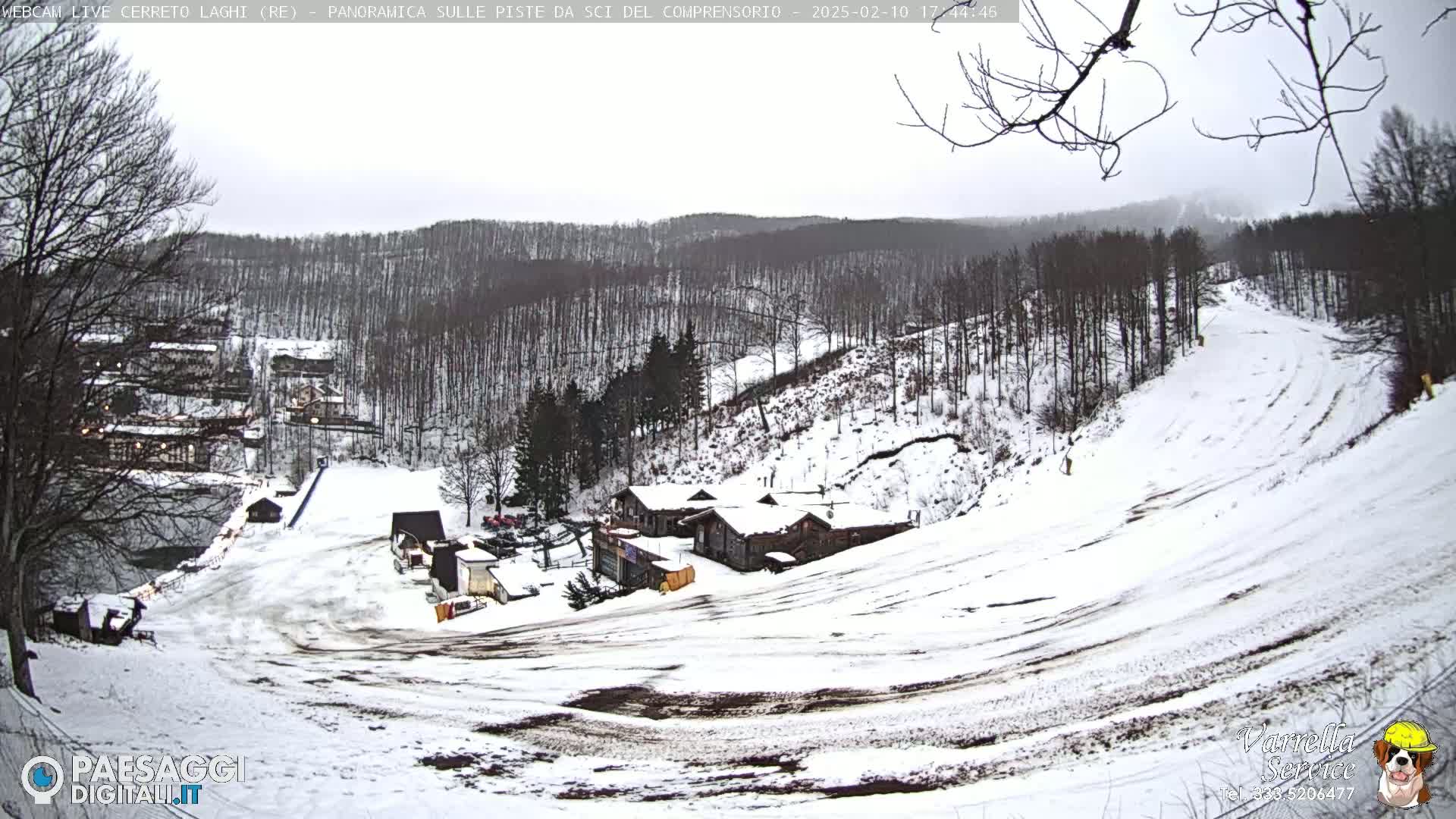 A snow-covered ski slope with several buildings at the bottom of the hill, under an overcast sky.