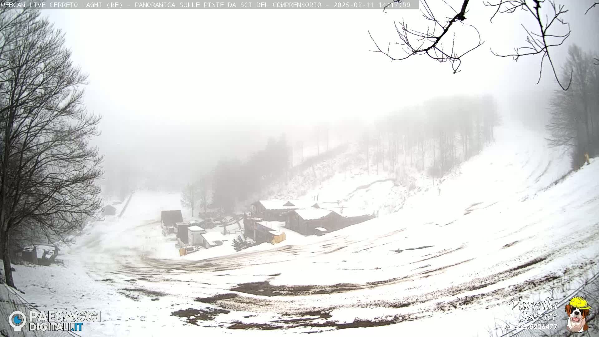 A snow-covered ski slope with several buildings is visible through a thick fog.