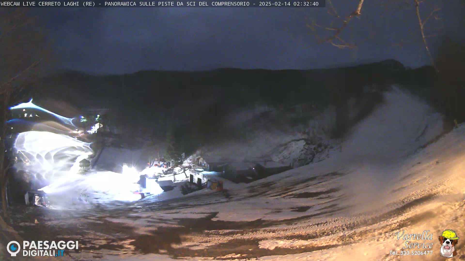 A nighttime view of a snow-covered ski slope with snowmaking equipment operating under a dark sky.