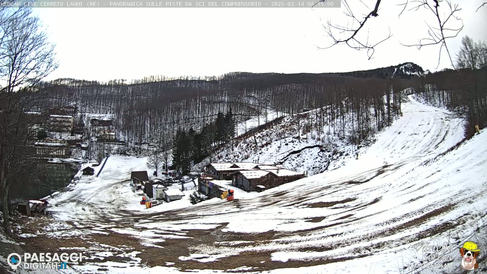 A snow-covered ski slope winds down a hill through a sparsely wooded area, with several small buildings visible near the bottom.