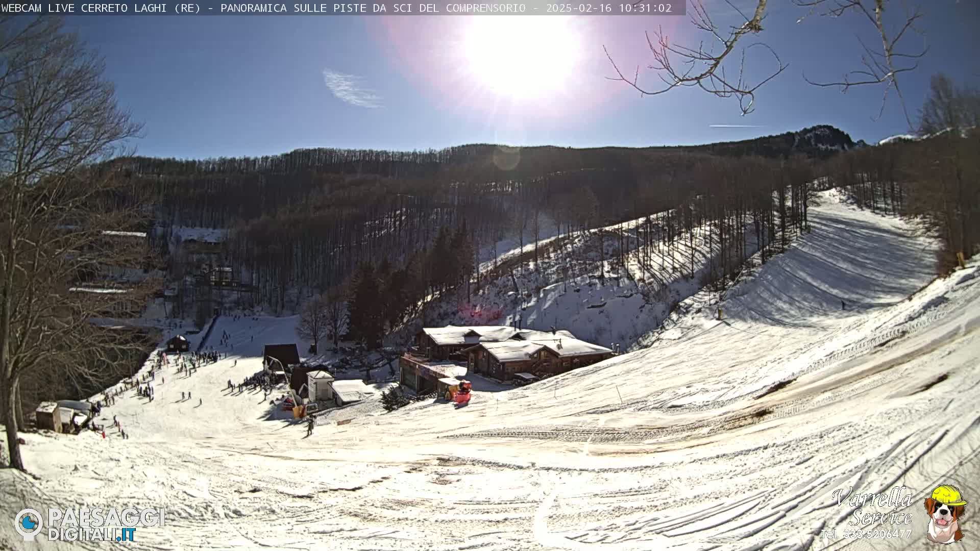 A sunny day at a snow-covered ski resort, showing several ski slopes, a lodge, and skiers on the runs.
